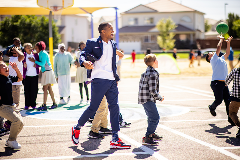 Josh Barringer, Call Me MISTER student, on the basketball court at an elementary school amongst a group of students, smiling.